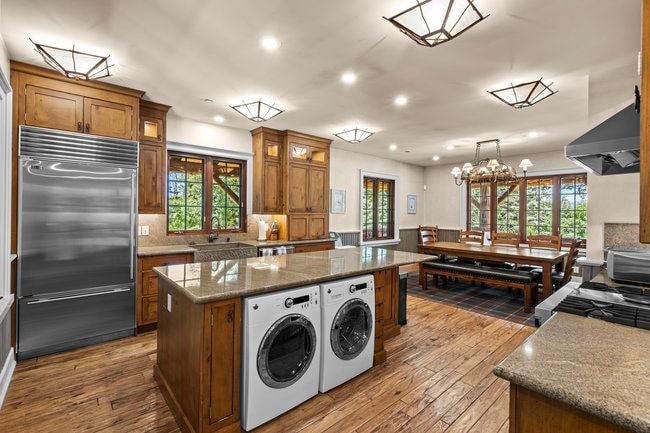 Spacious kitchen featuring wood-finish flooring, custom wood cabinetry, stainless steel appliances, and stone countertops