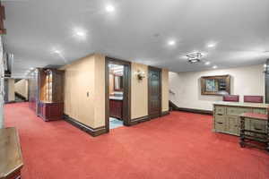 Spacious room featuring red patterned carpeting, recessed lighting, and dark wood-stained trim
