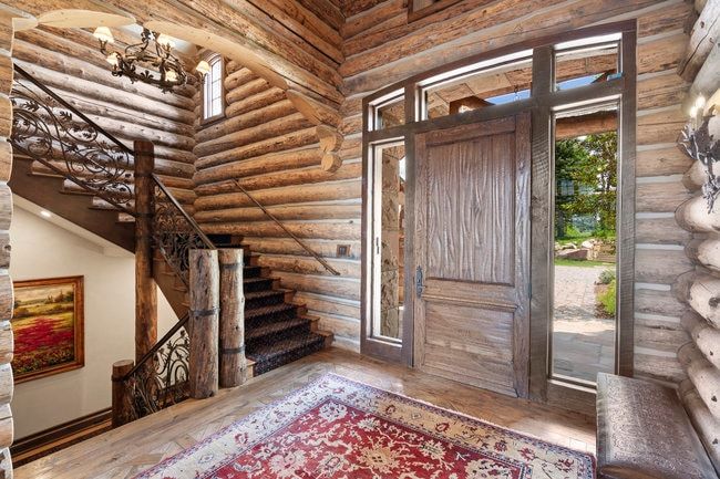 Log construction entry with a substantial wood door, transom and sidelight windows, a grand staircase with wrought iron railing, and wood-finish flooring