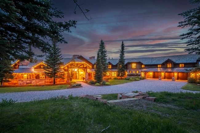 Expansive log-style residence featuring a stone-clad foundation and multiple garage bays
