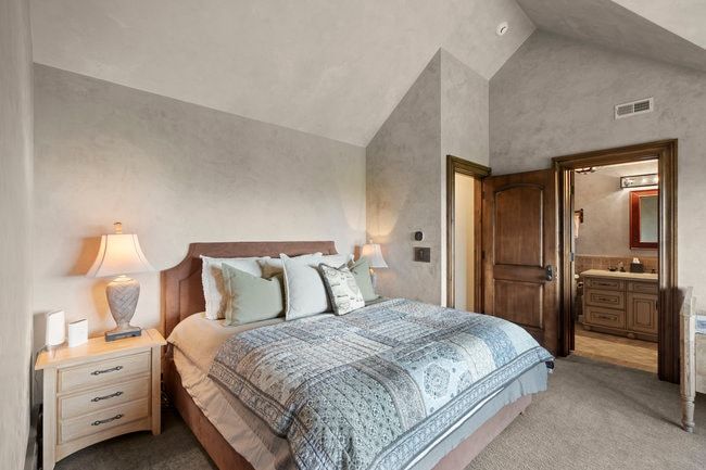 Vaulted ceilings and textured wall finishes define this room, featuring a wood-finish door and a visible en-suite bath with a wood-finish vanity