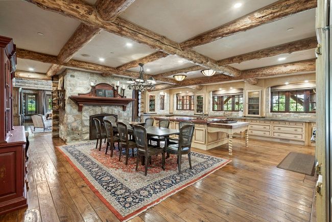 Kitchen and dining area featuring wood-finish flooring, exposed wood beams, a stone fireplace, cream cabinetry, and recessed lighting