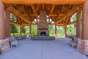Expansive covered patio featuring a stone fireplace, exposed timber beams, a vaulted wood ceiling, concrete flooring, and stone pillar bases