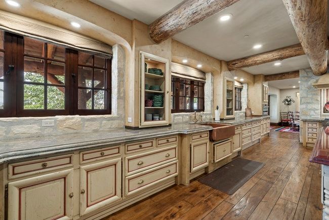 Spacious kitchen featuring extensive cabinetry, wood-finish flooring, a copper farmhouse sink, recessed lighting, and exposed ceiling beams