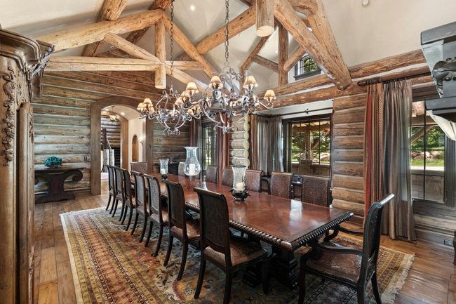 Vaulted ceiling with exposed wood beams, log wall construction, wood-finish flooring, ornate chandelier, and multiple window exposures