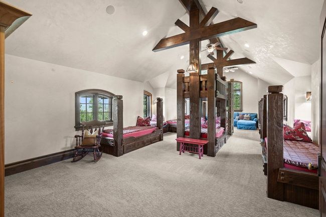 Spacious room featuring multiple custom built-in wood bunk beds, vaulted ceilings with exposed wood beams, recessed lighting, and arched windows providing natural illumination