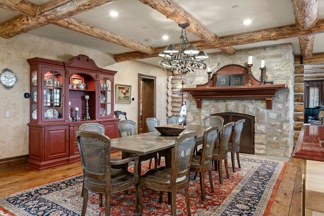 Dining area featuring a stone fireplace with a wood mantel, exposed log ceiling beams, and wood-finish flooring