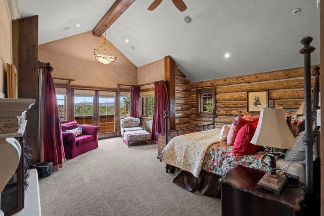 Vaulted ceiling featuring a wood beam, log wall construction, French doors opening to an outdoor area, recessed lighting, and a stone fireplace