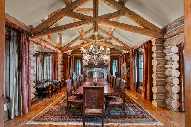 Vaulted ceiling with exposed wood beams, log wall construction, wood-finish flooring, stone-clad fireplace with mantel, and an ornate chandelier