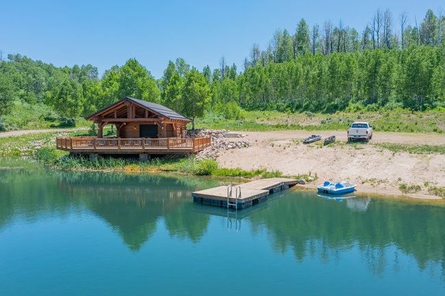 Waterfront log structure featuring a spacious wrap-around deck, private dock, and surrounding greenery