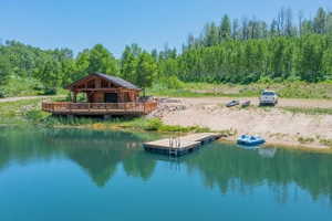Waterfront log structure featuring a spacious wrap-around deck, private dock, and surrounding greenery