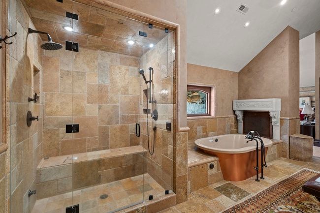 Spacious bathroom featuring a glass-enclosed shower with stone tile, a built-in shower bench, and multiple shower heads