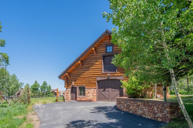 Rustic log cabin structure with a stone foundation, a pitched roof, and two large barn-style doors