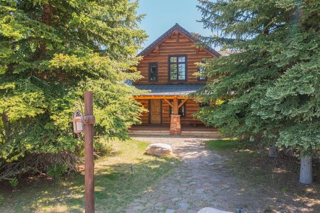Log cabin style exterior featuring a covered porch, stone column accents, and a dark shingle roof