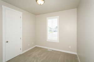 Carpeted room featuring a white paneled door, a window with white louvered shutters, and a ceiling-mounted light fixture