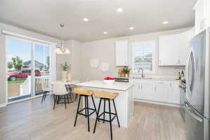 Modern kitchen featuring an island with seating, stainless steel appliances, white cabinetry, and light wood-finish flooring
