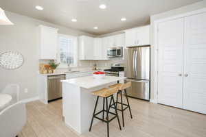 Modern kitchen featuring a central island, white cabinetry, stainless steel appliances, and light wood-finish flooring
