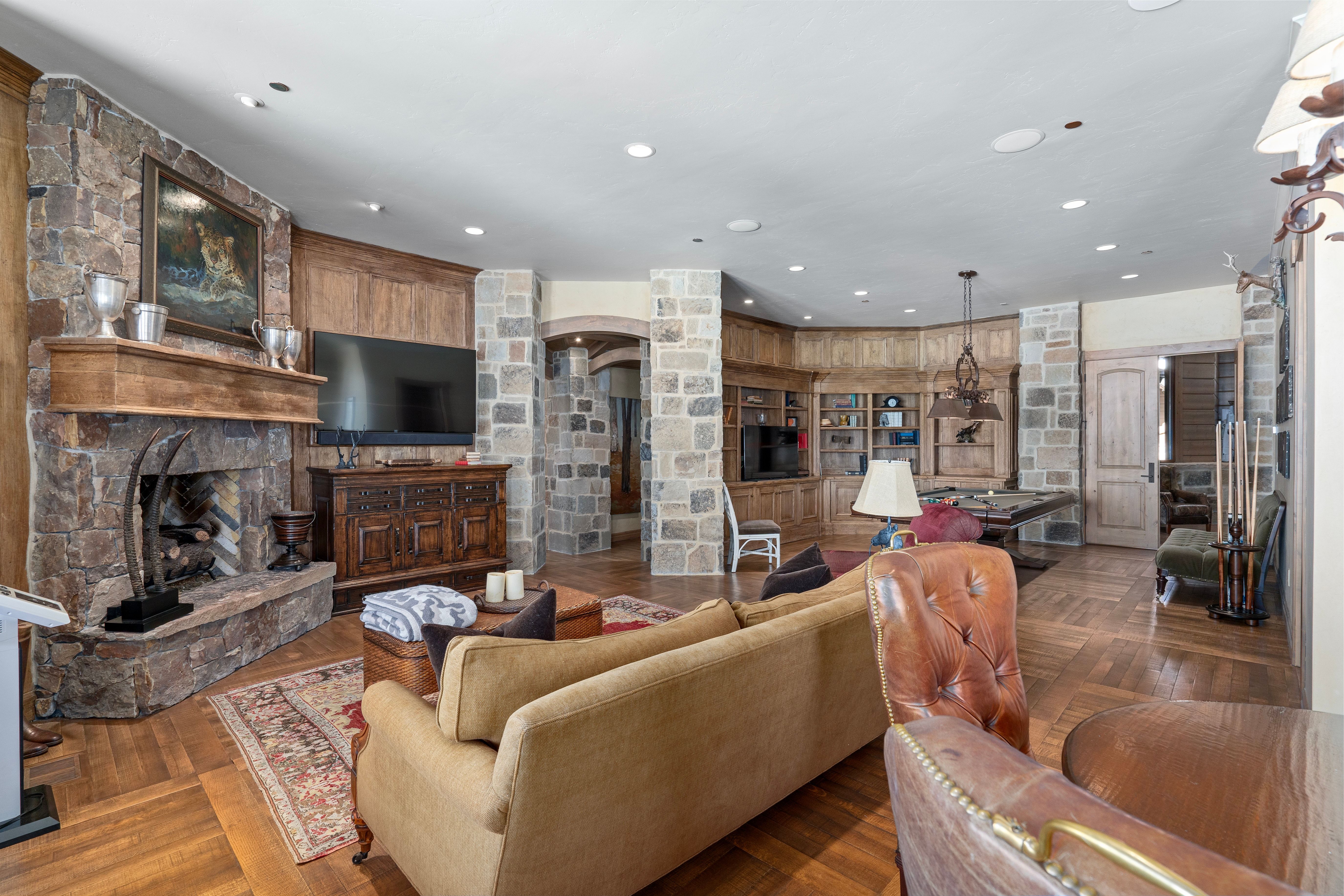 Stone-clad fireplace with a substantial hearth and wood mantle, complemented by recessed lighting and wood-finish flooring