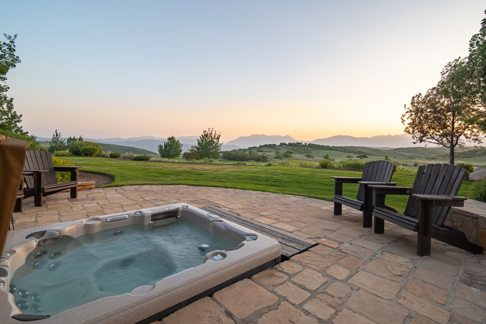Stone patio featuring an in-ground hot tub, expansive lawn, and distant mountain scenery