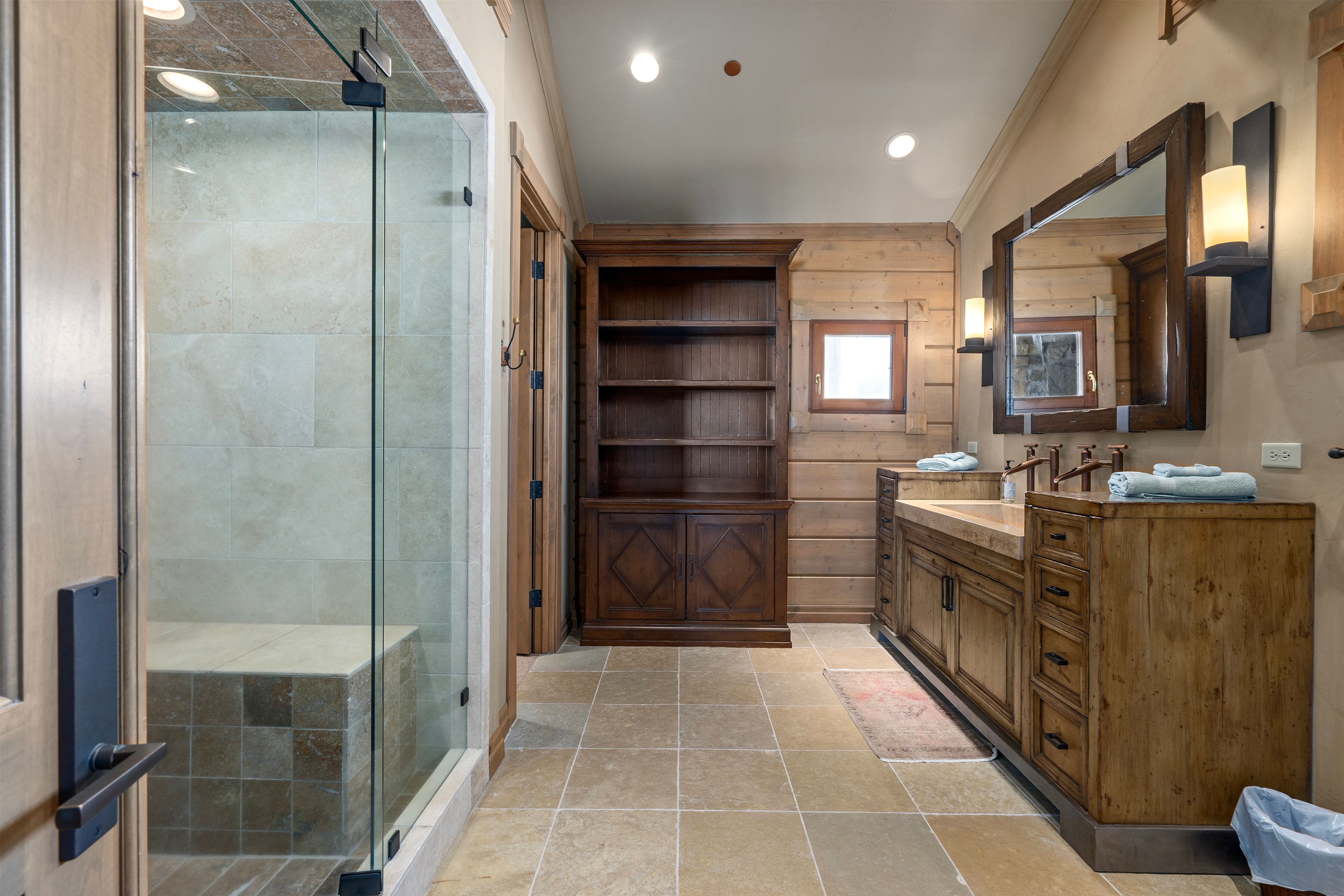 Bathroom featuring a glass-enclosed shower with tile surround and built-in bench, a dual vanity with wood-finish cabinetry, a large framed mirror, and recessed lighting