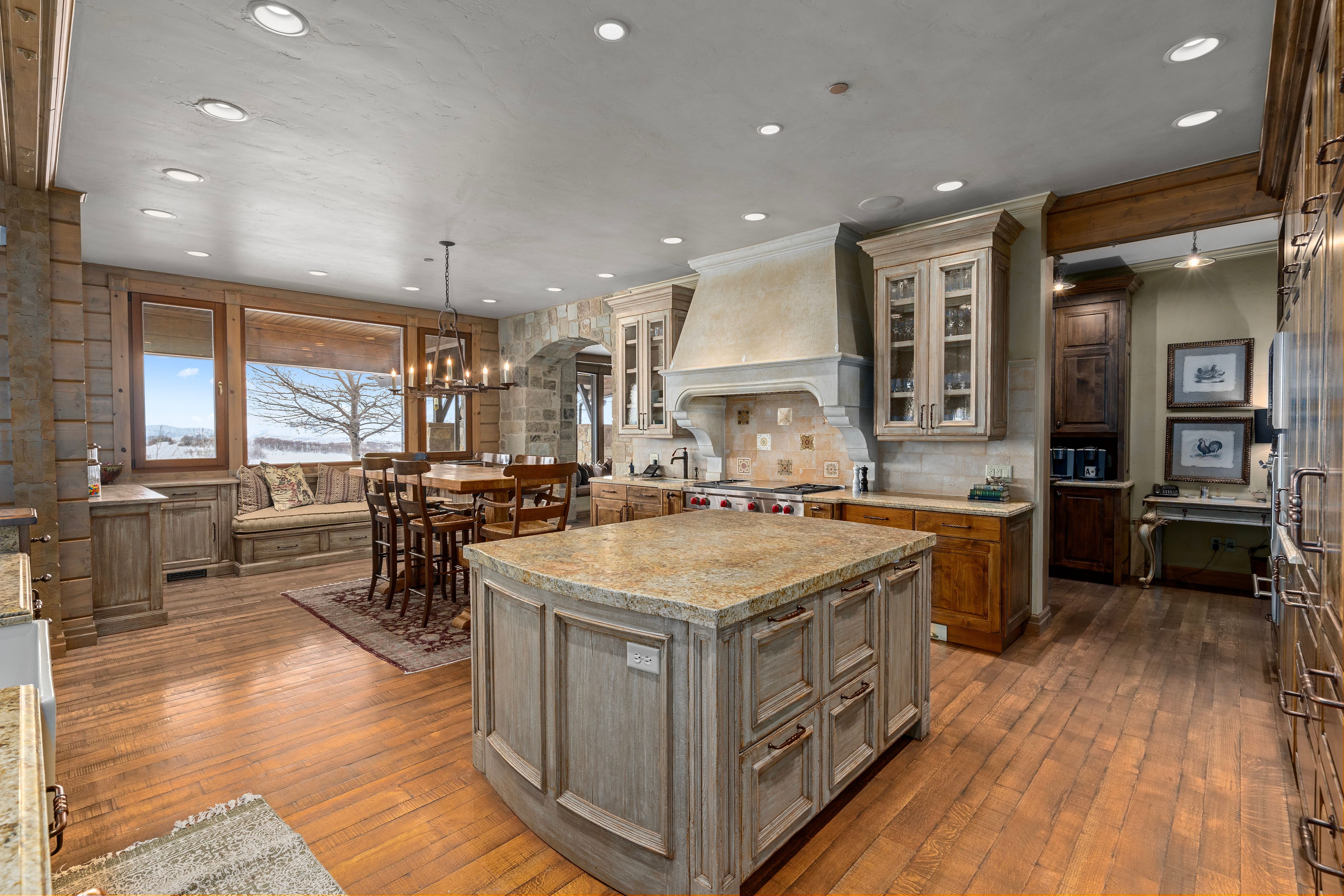 Gourmet kitchen featuring a large stone-finish island with granite countertop, wood-finish flooring, custom cabinetry, recessed lighting, and a built-in banquette