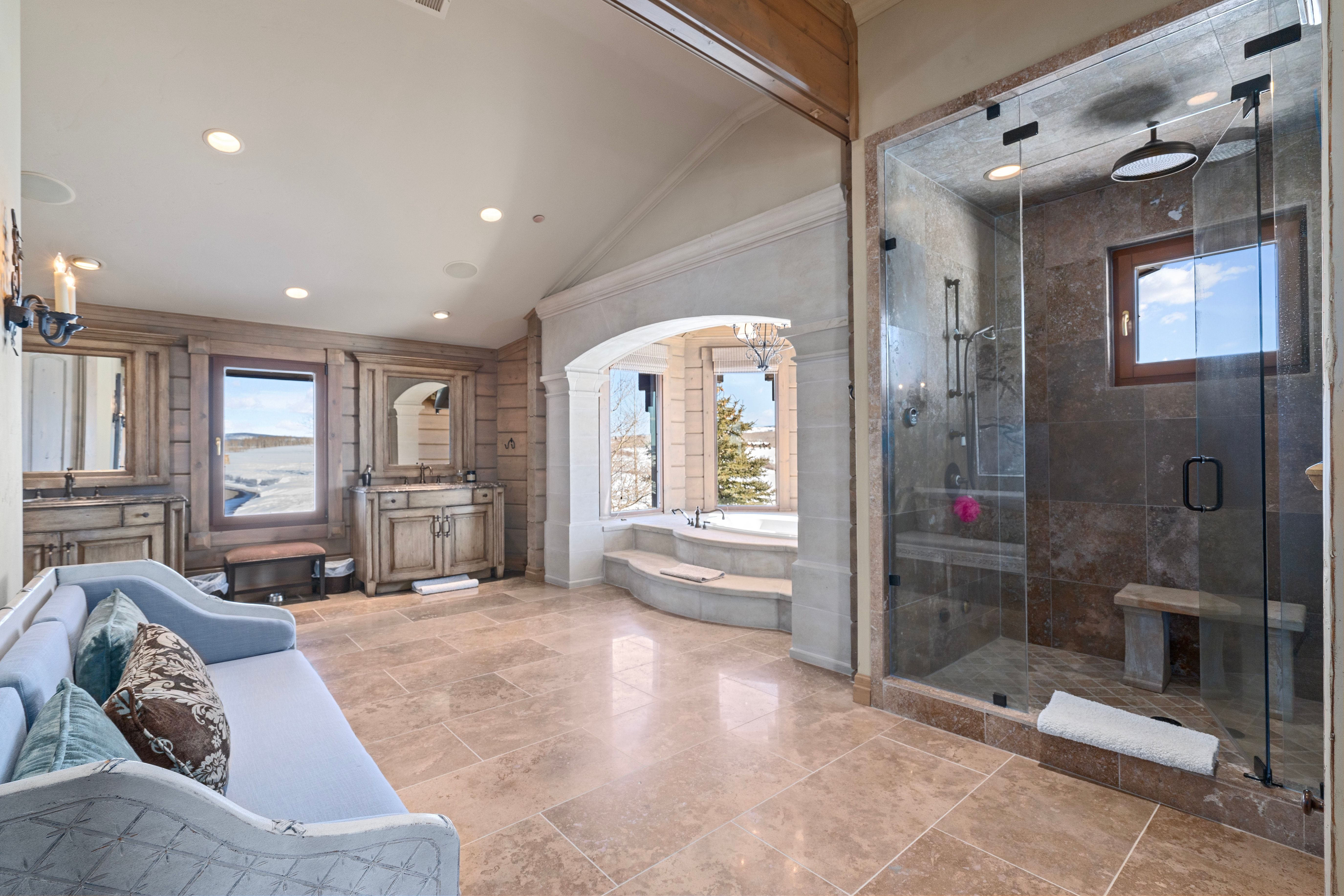Spacious bathroom featuring stone tile flooring, a large glass-enclosed shower with a built-in bench, and a jetted soaking tub
