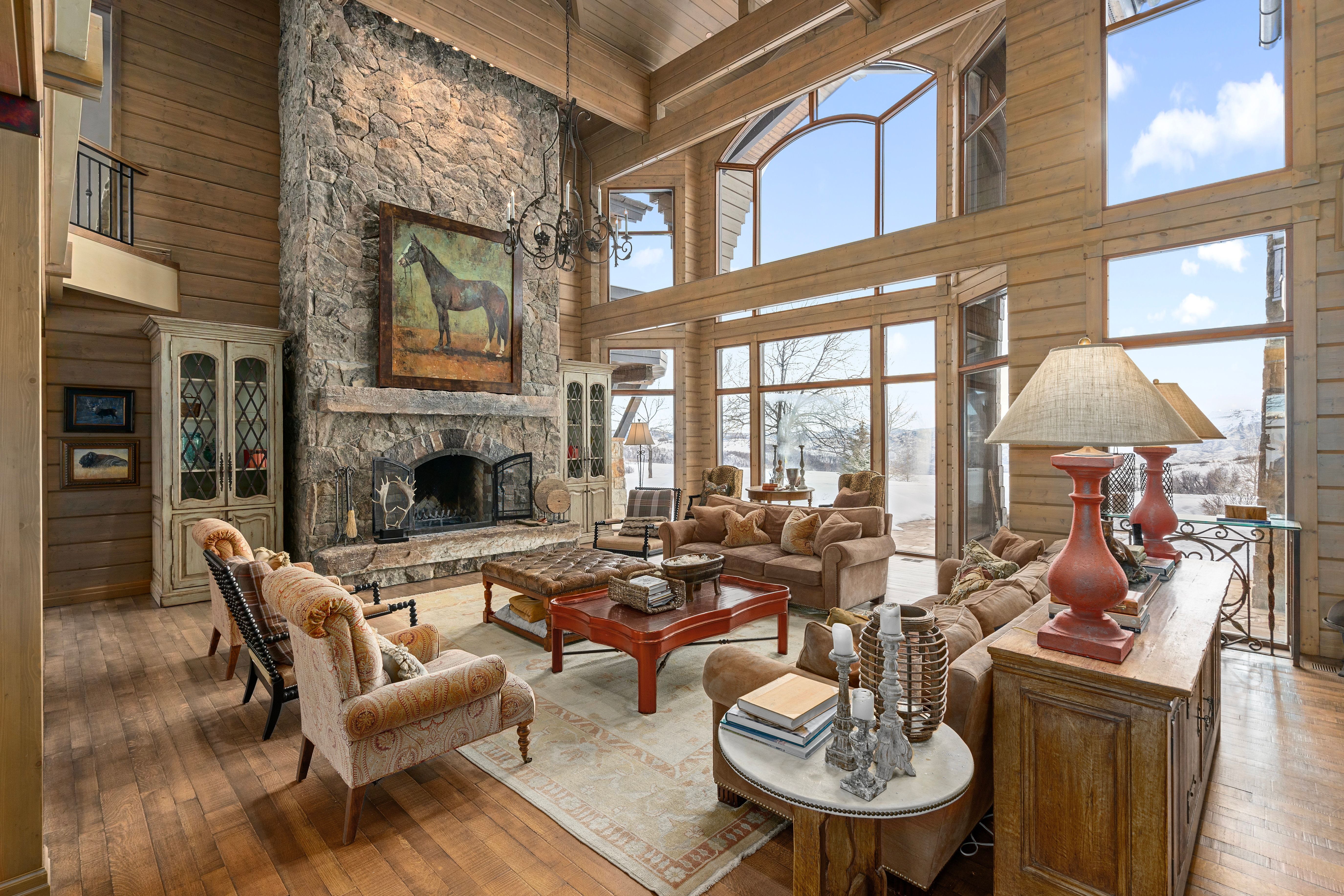 Great room featuring a floor-to-ceiling stone fireplace, soaring wood-paneled walls, exposed wood beams, expansive windows, and wood-finish flooring