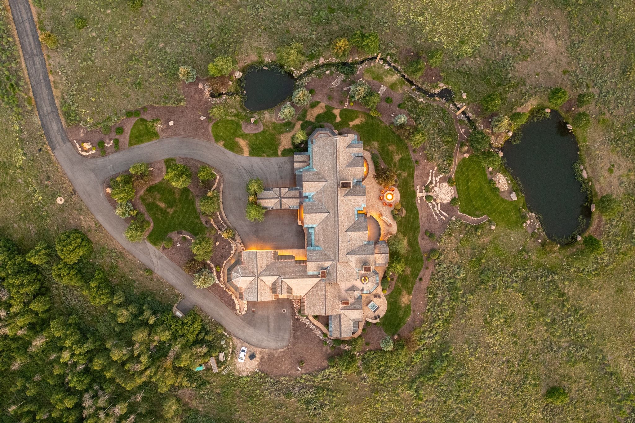 Expansive estate featuring a multi-level roofline, extensive paved driveway, two distinct ponds, a meandering stream, and landscaped grounds