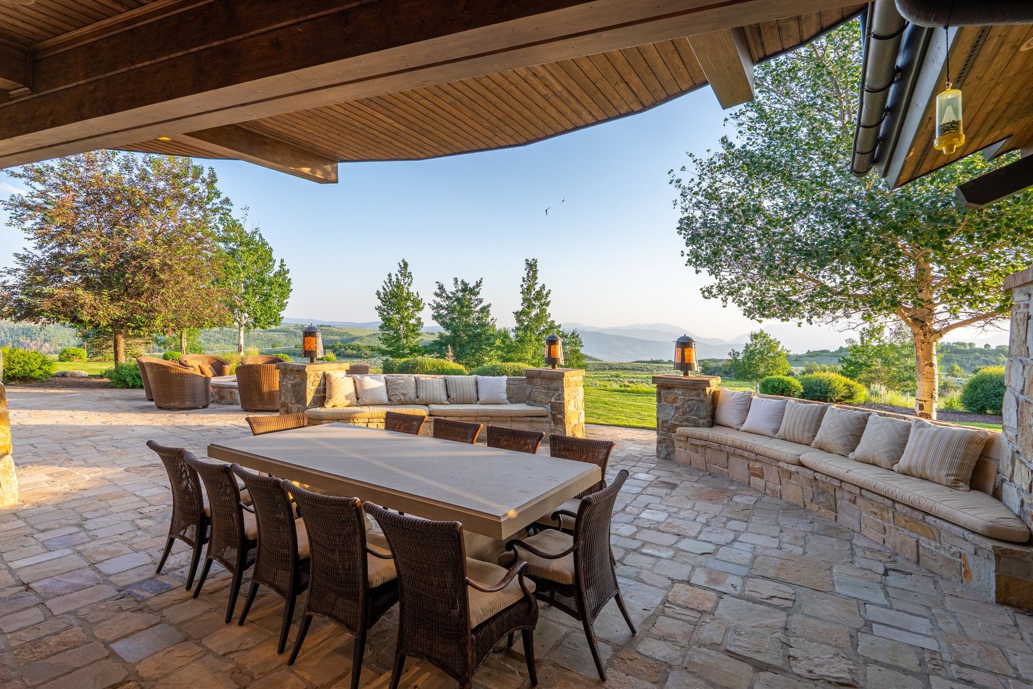 Expansive stone patio featuring a dining area, a built-in stone bench with cushions, and a separate seating area