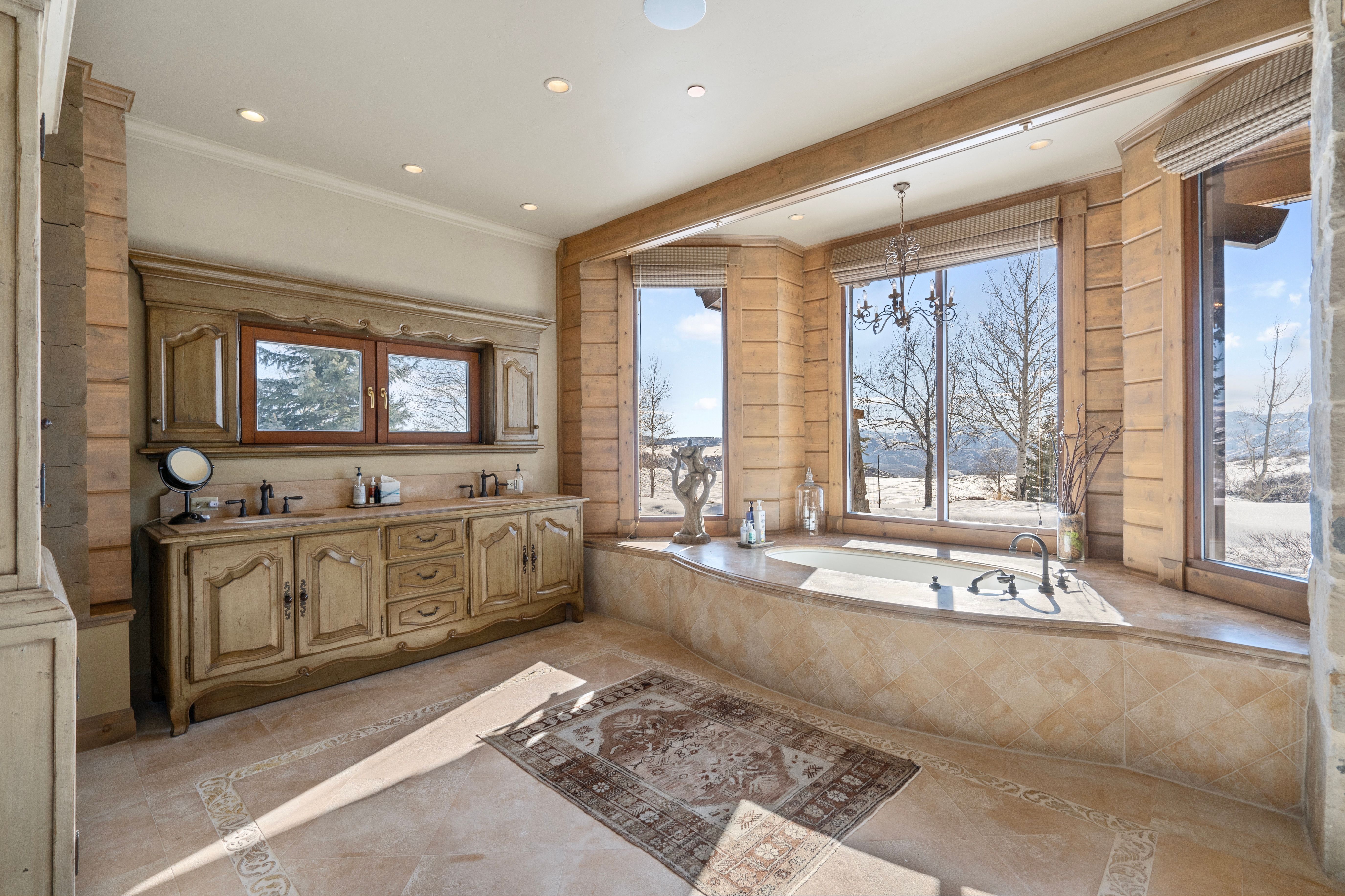 Soaking tub with multiple large windows, recessed lighting, and an ornate chandelier