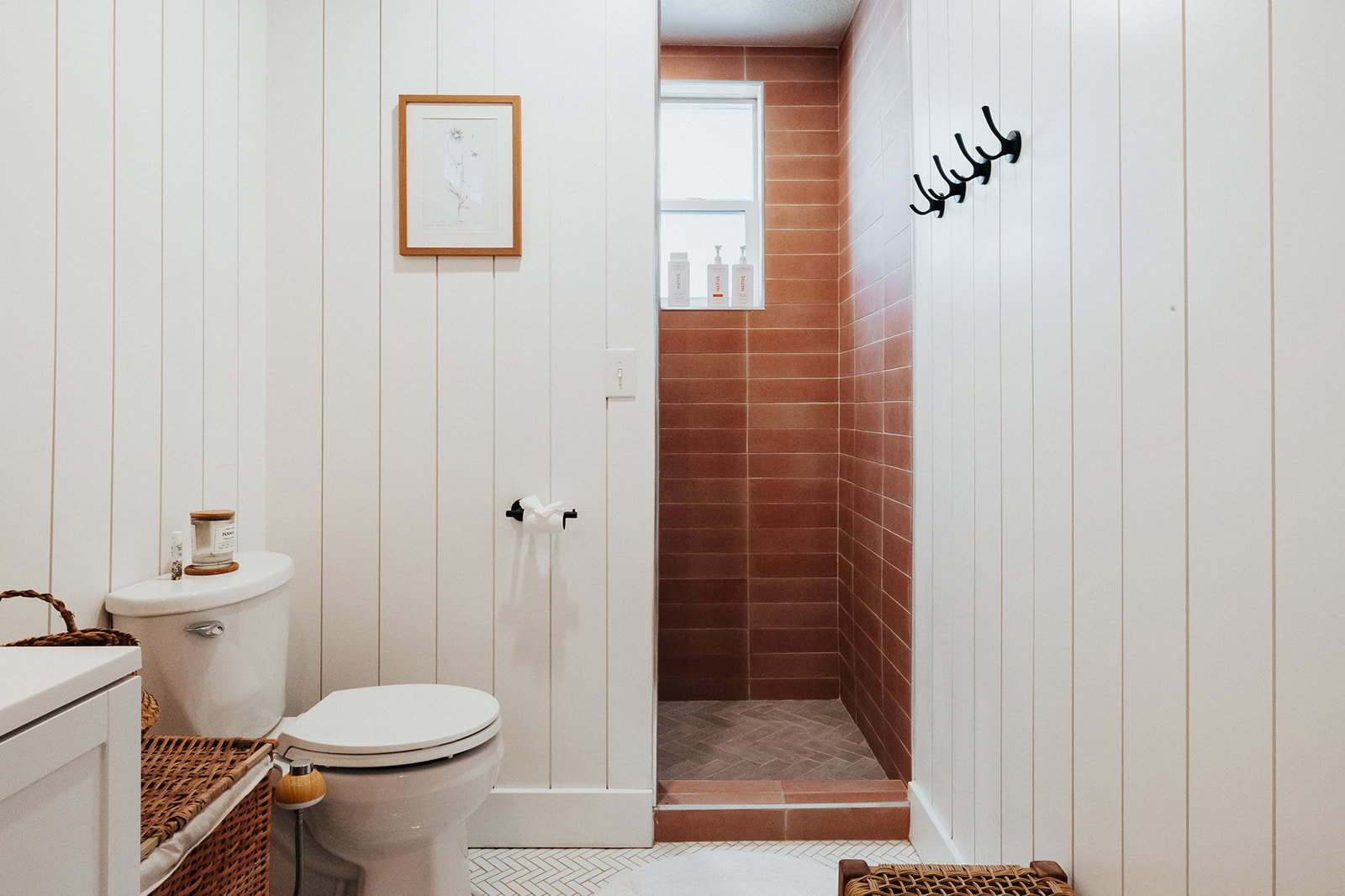 Bathroom featuring vertical white shiplap walls, a toilet with a white tank, and a walk-in shower with terra cotta subway tile and a coordinating herringbone tile floor