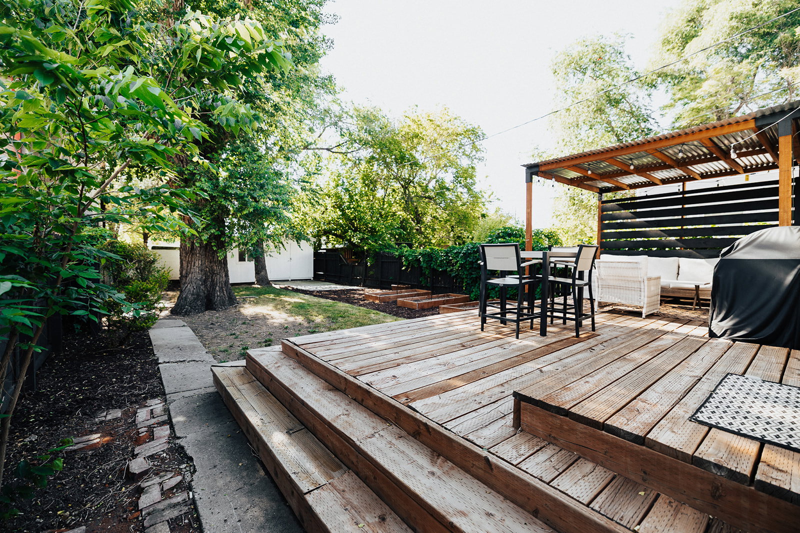 Expansive multi-level wood deck featuring a covered pergola with a corrugated roof