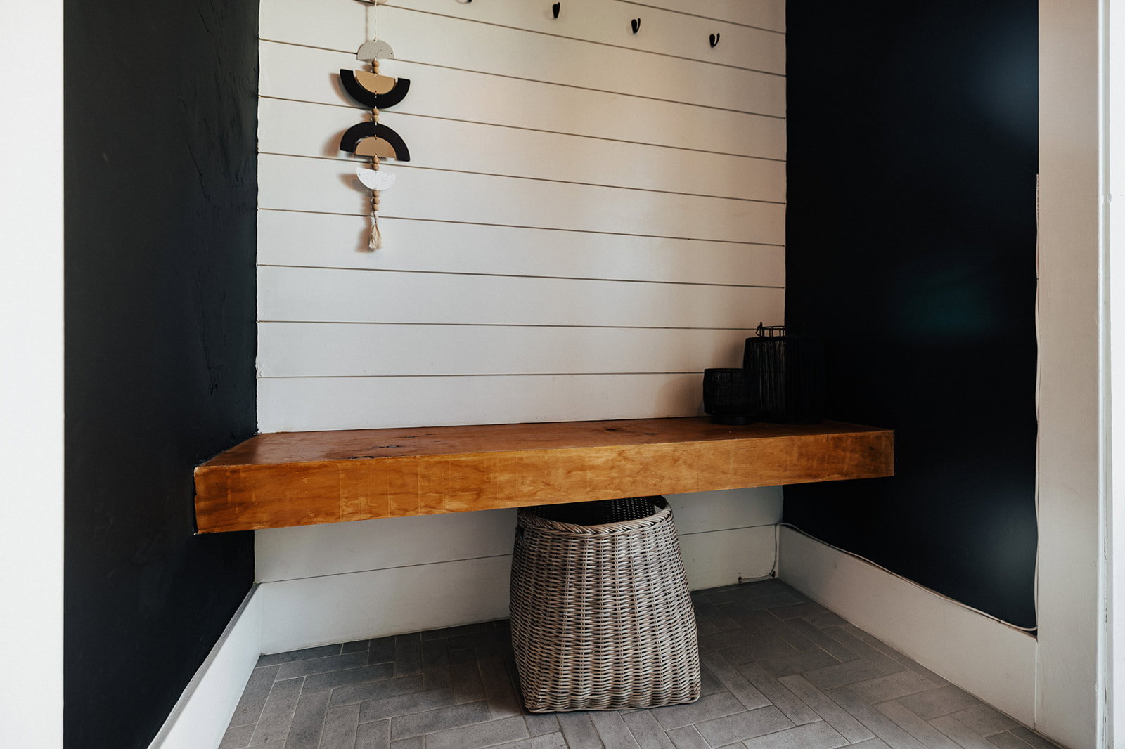 Entryway nook featuring white shiplap walls, a rich wood-finish floating bench, dark accent walls, and herringbone pattern floor tiles