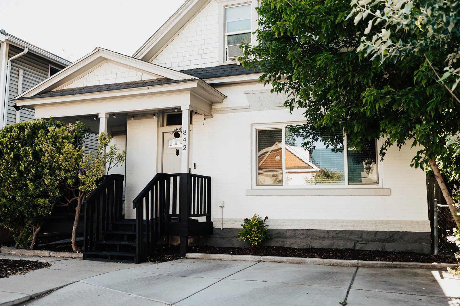 White brick exterior featuring a covered porch with black railing and steps, a white front door, and a prominent front window