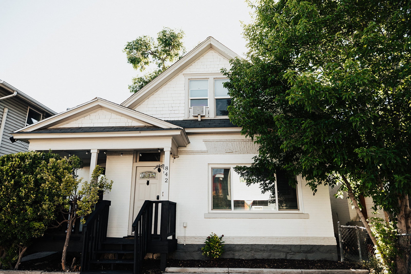 White exterior with shingle siding on the gable, a covered front porch, and black painted porch railings