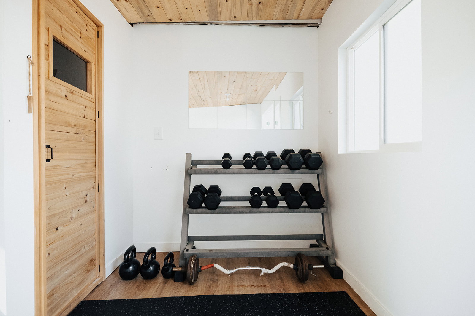 Room featuring a light wood-finish ceiling, a natural wood door with a rectangular window, and a single window with white trim