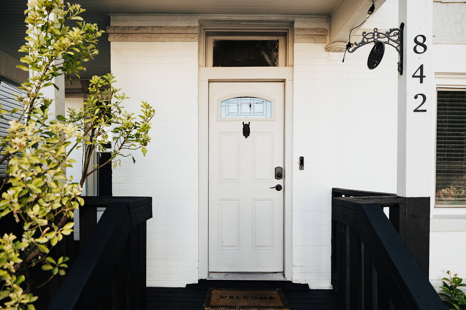 Entryway featuring a white paneled door with an arched window, black railings, and a brick exterior with address numbers