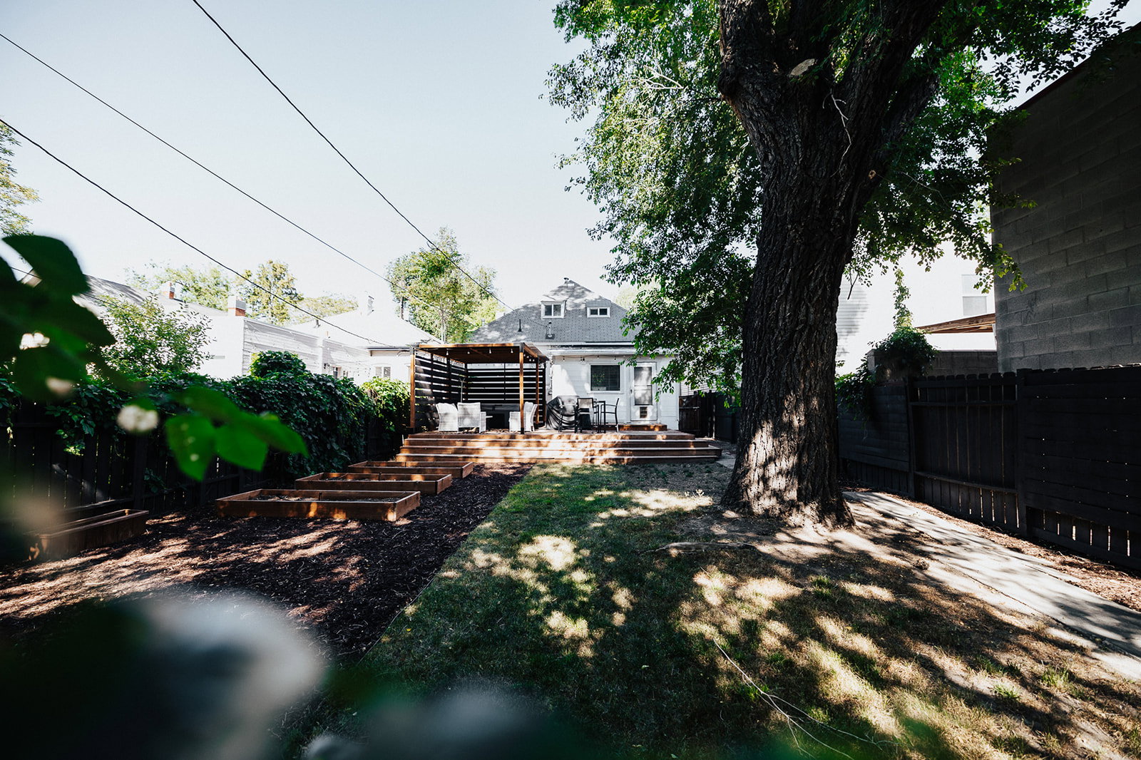 Expansive backyard featuring a multi-level wood deck, a wood pergola, built-in raised garden beds, a mature tree, and a manicured lawn