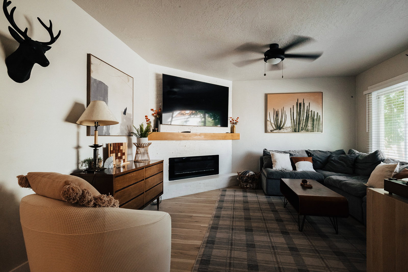 Living area featuring a corner fireplace with a wood mantle, wood-finish flooring, and a ceiling fan