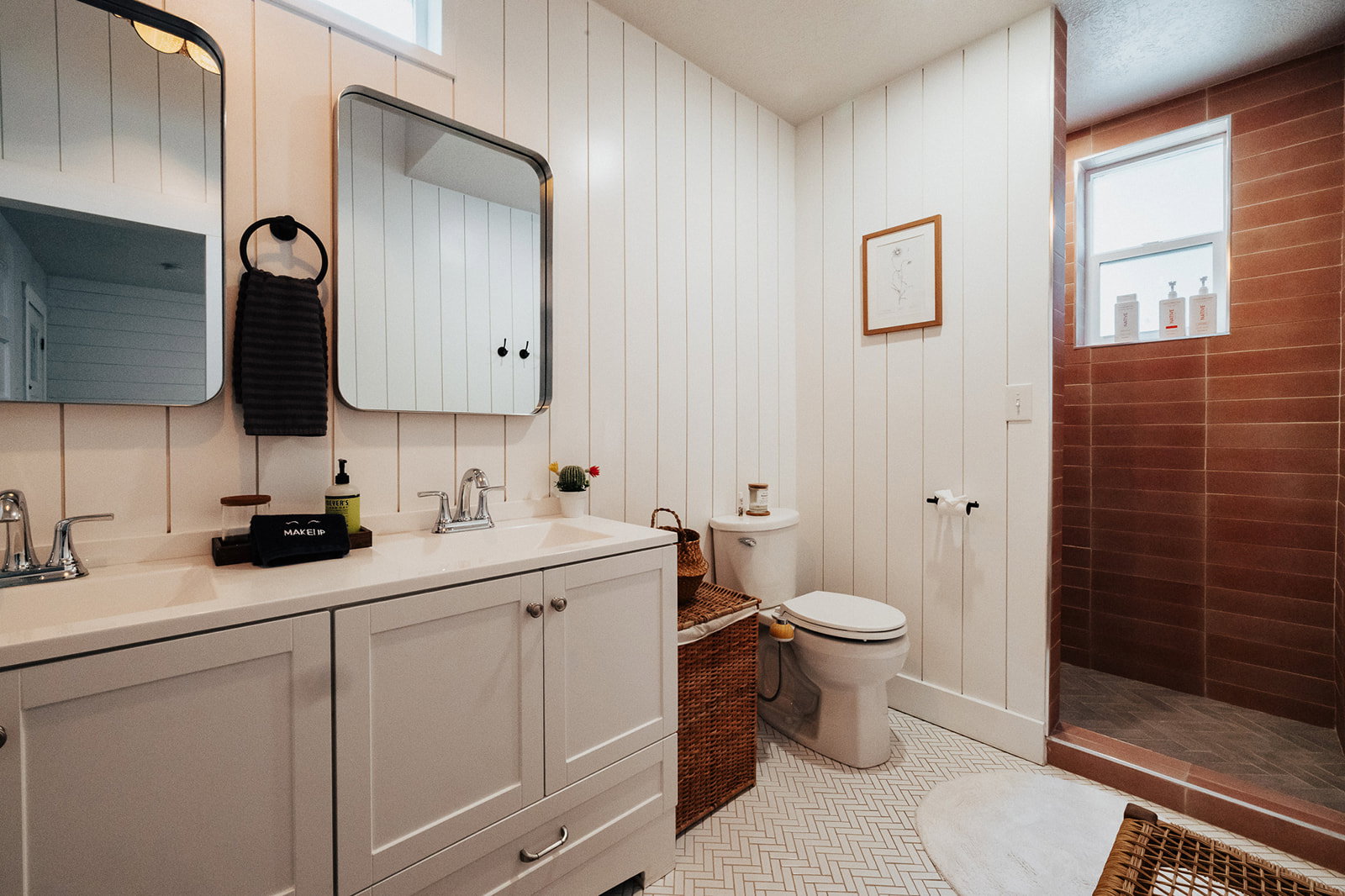 Bathroom featuring a double vanity with light-colored cabinetry and chrome fixtures, white shiplap walls, and a herringbone-patterned floor