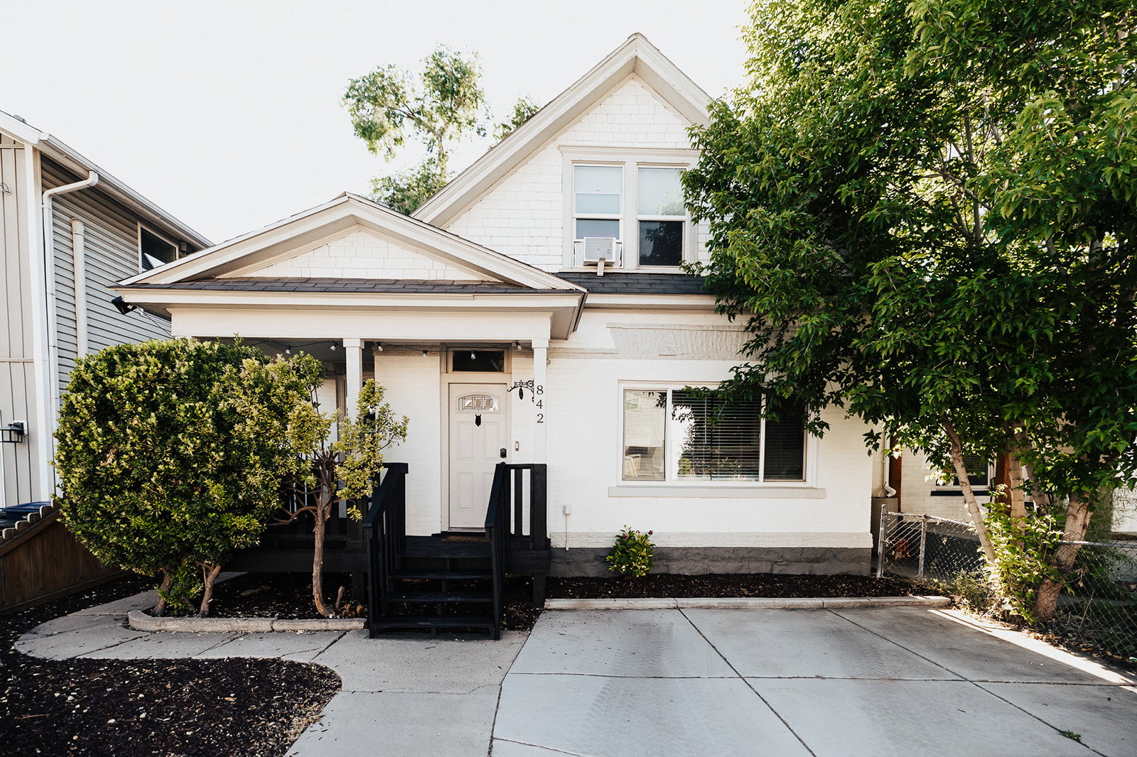 White exterior featuring a covered porch with black steps, a concrete driveway, and mature landscaping
