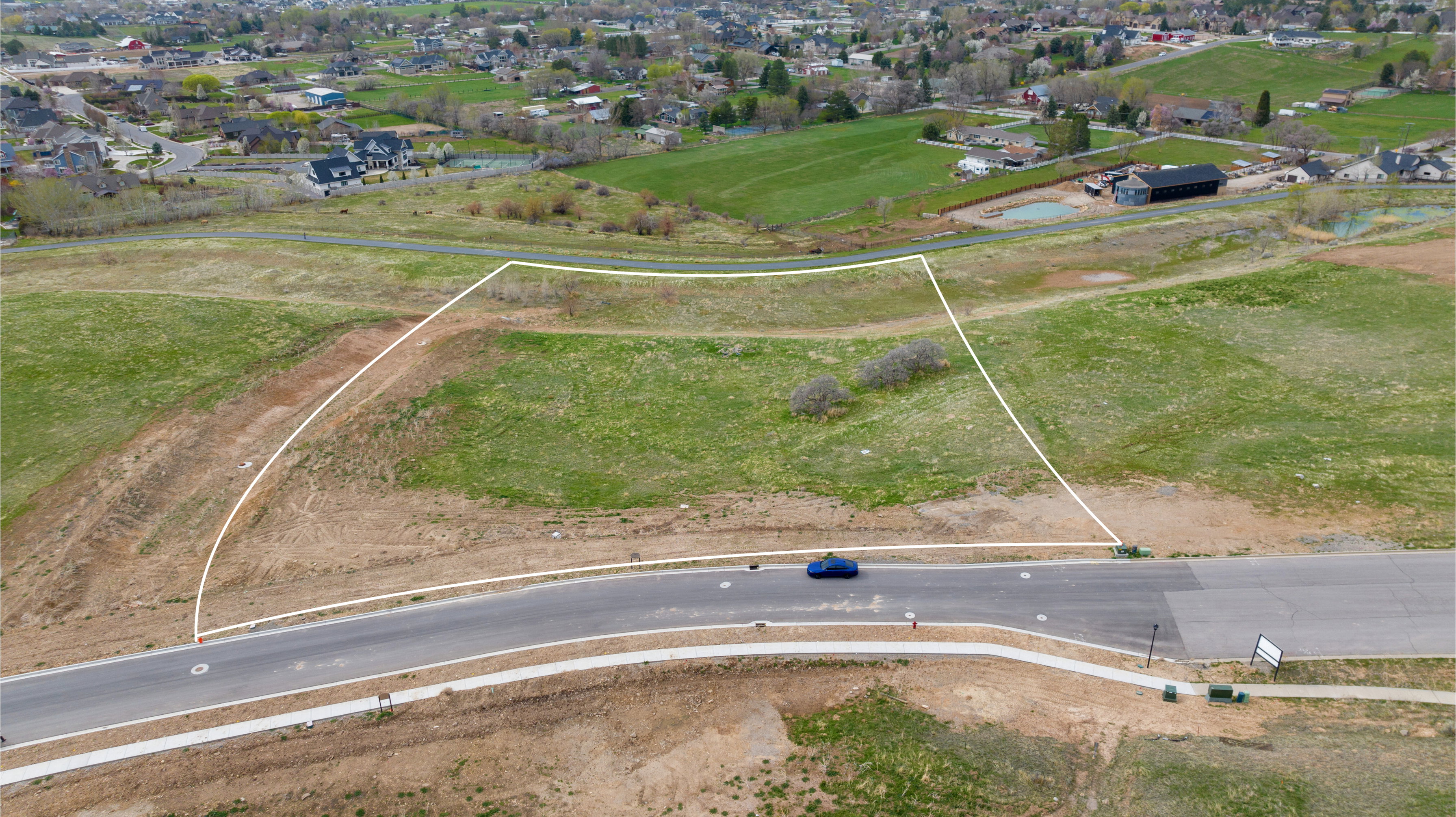 Expansive lot featuring a curvilinear paved road, concrete sidewalk, gentle slopes, and existing vegetation