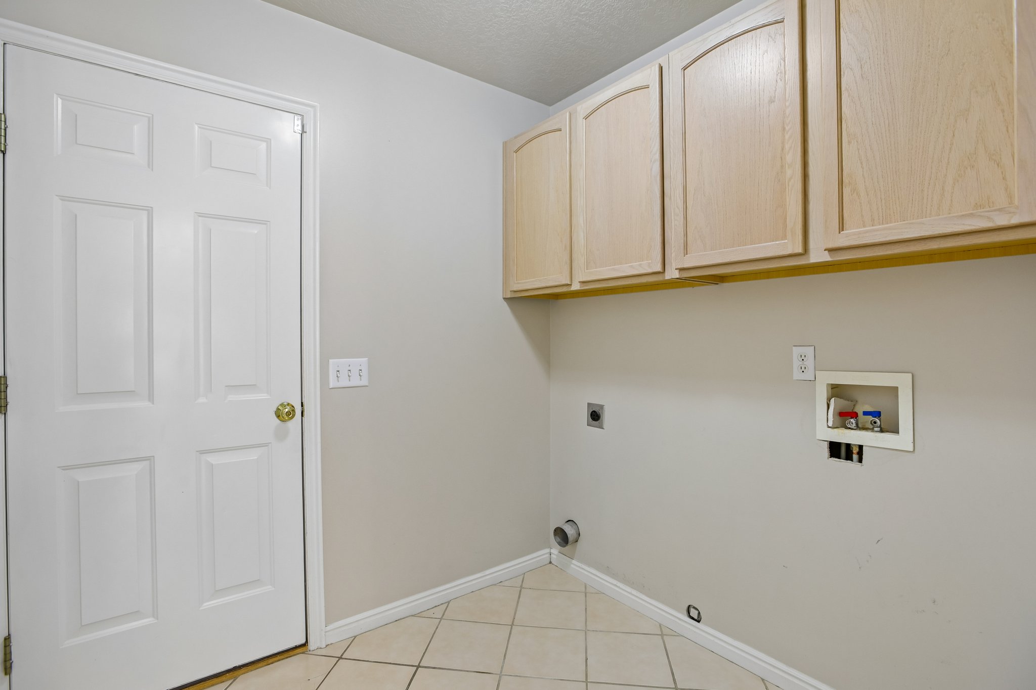 Utility space featuring overhead cabinetry with arched panel doors, tile flooring, and light neutral wall paint