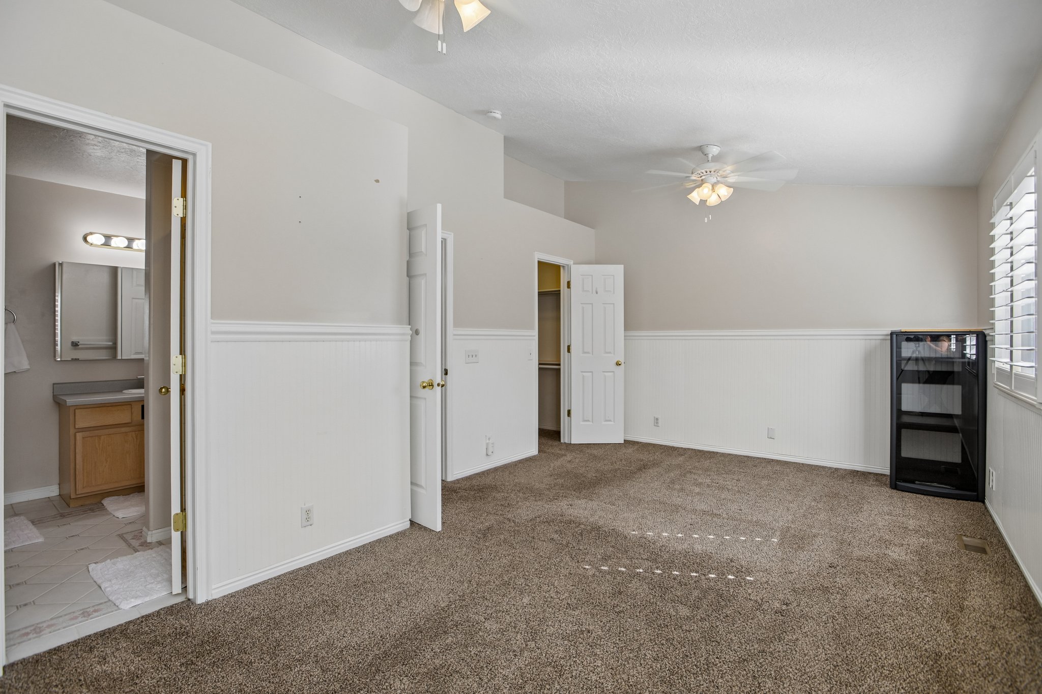 Spacious room featuring vaulted ceilings, ceiling fan light fixture, wainscoting, and carpet flooring