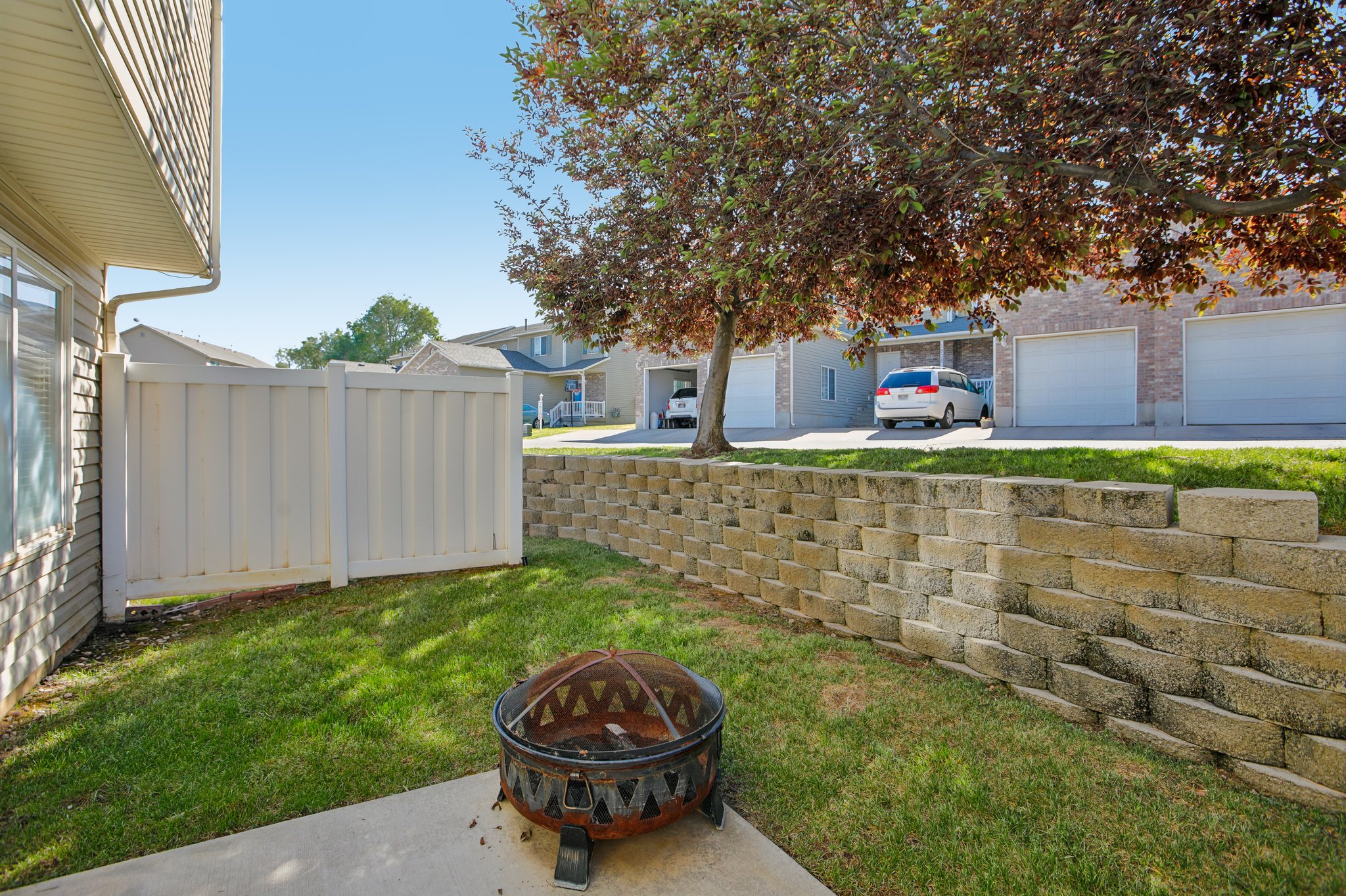 Private fenced patio area featuring a concrete slab, green lawn, and a tiered stone retaining wall