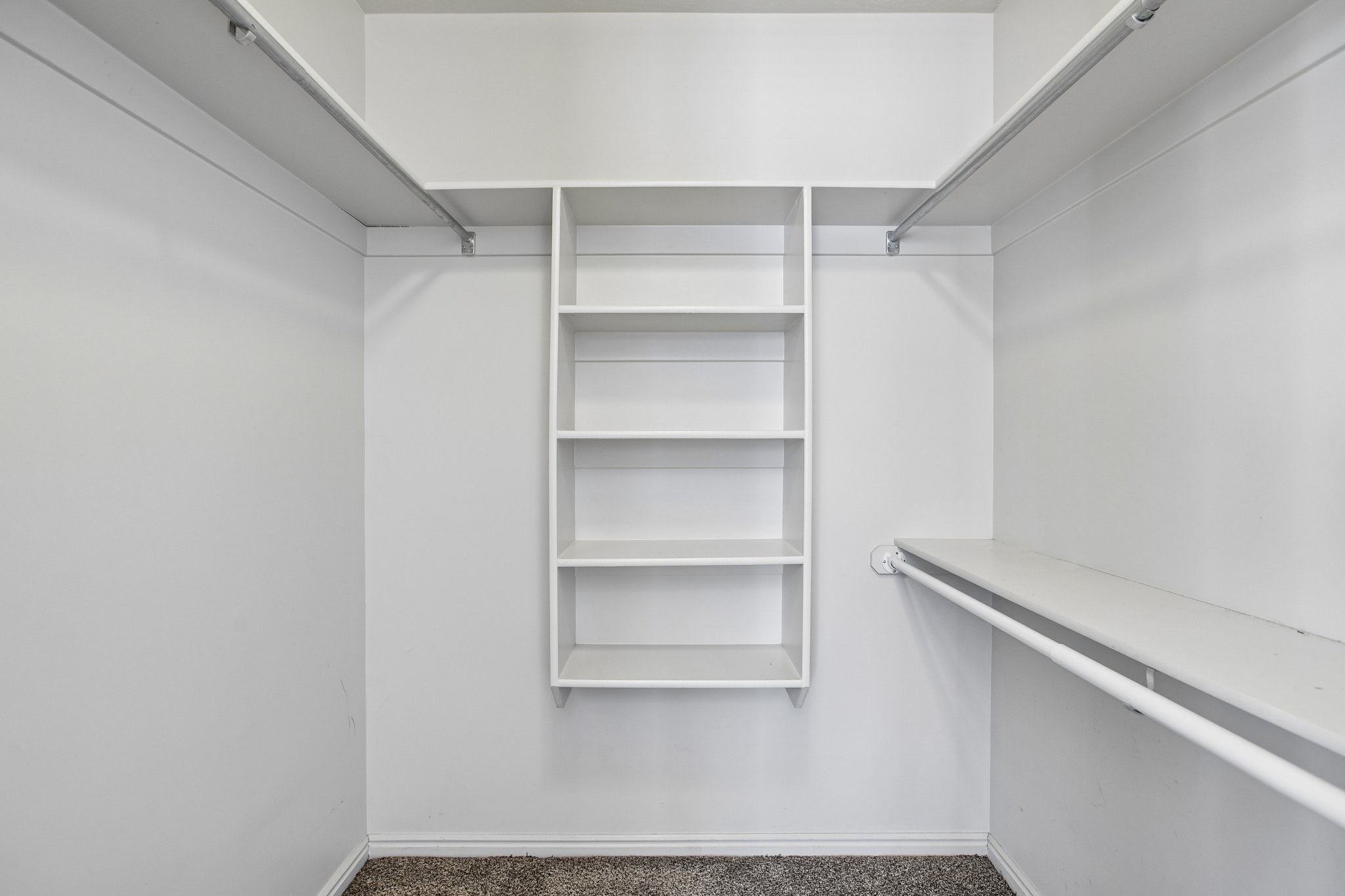 Walk-in closet featuring built-in shelving, multiple hanging rods, and neutral-toned carpeting