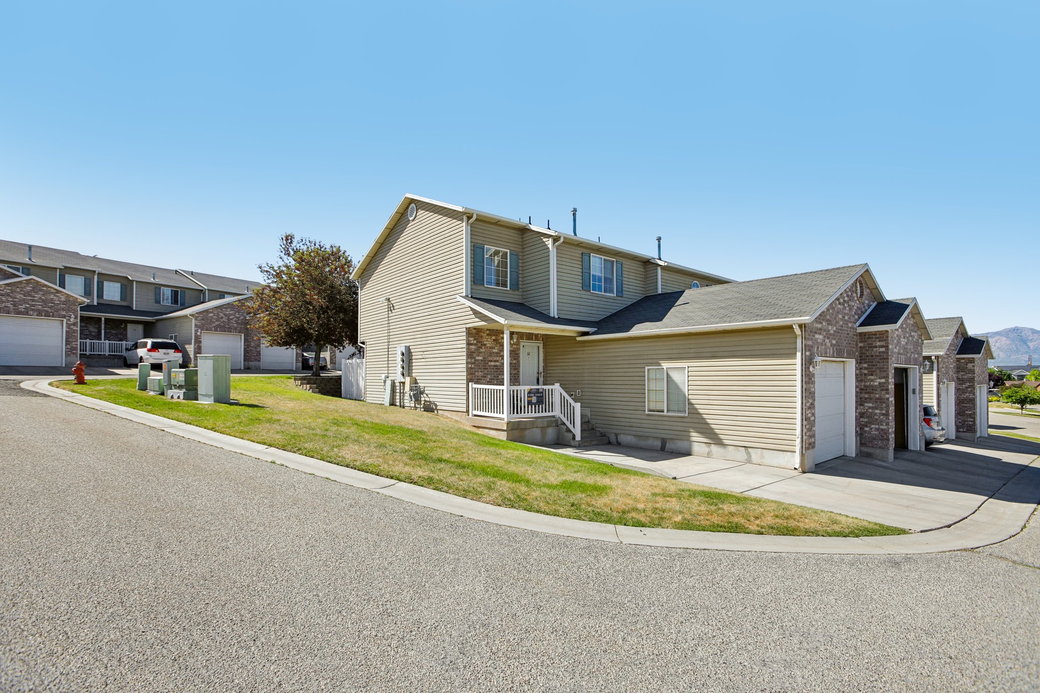 Townhome exterior featuring tan siding, brick accents, and a covered front porch