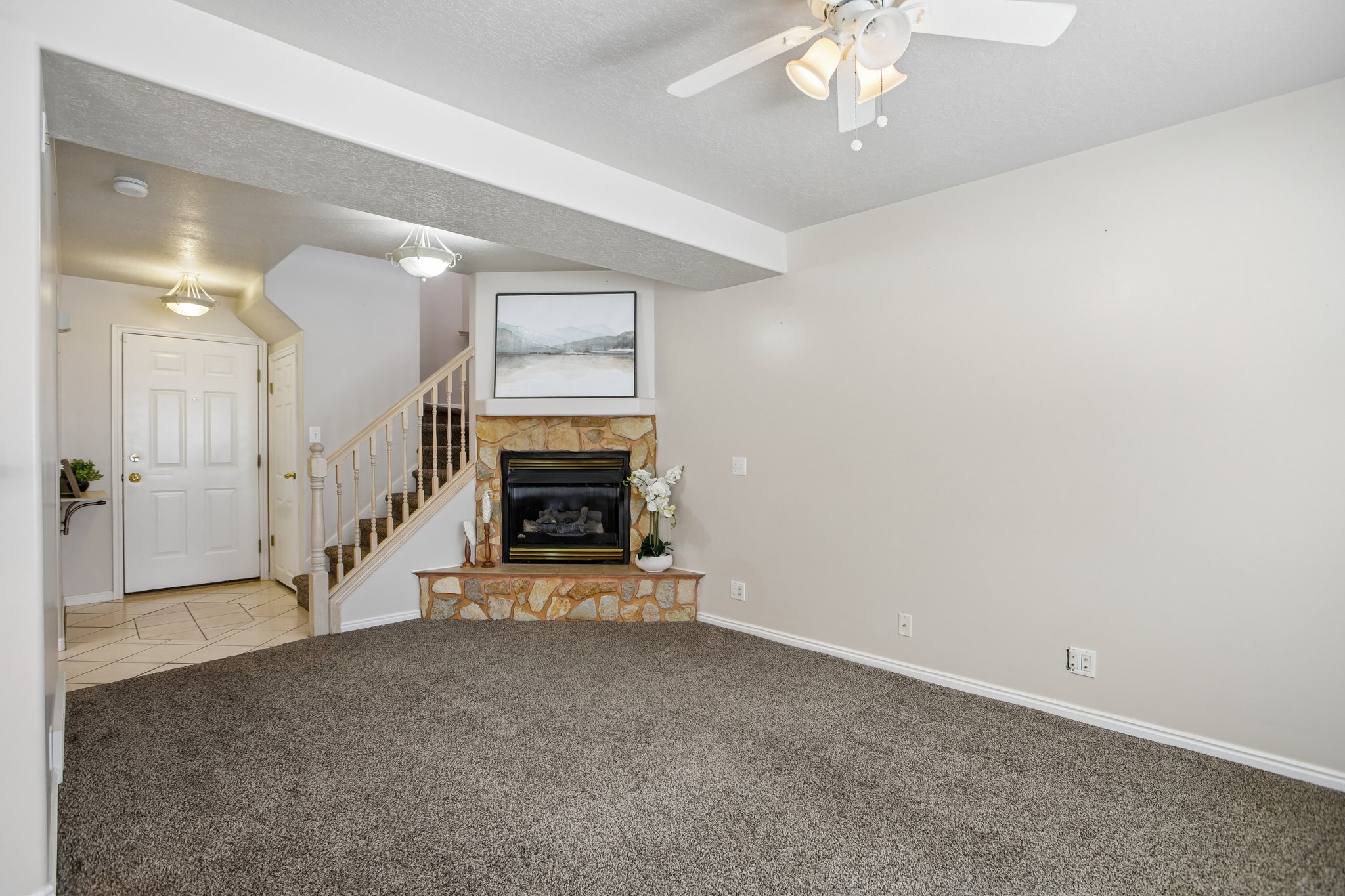 Stone-clad fireplace with a black insert, carpeted flooring, and a ceiling fan with integrated lighting