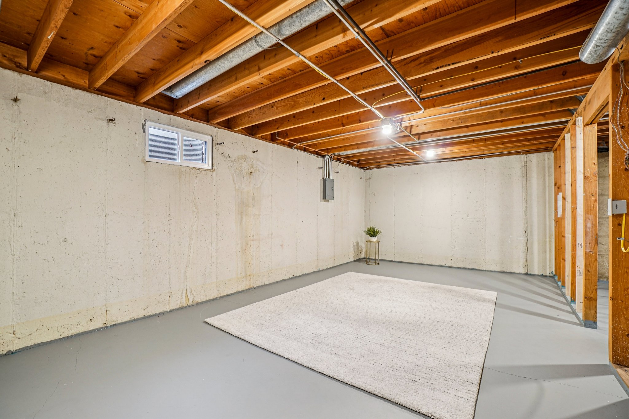 Unfinished lower level featuring exposed wood ceiling joists and painted concrete flooring