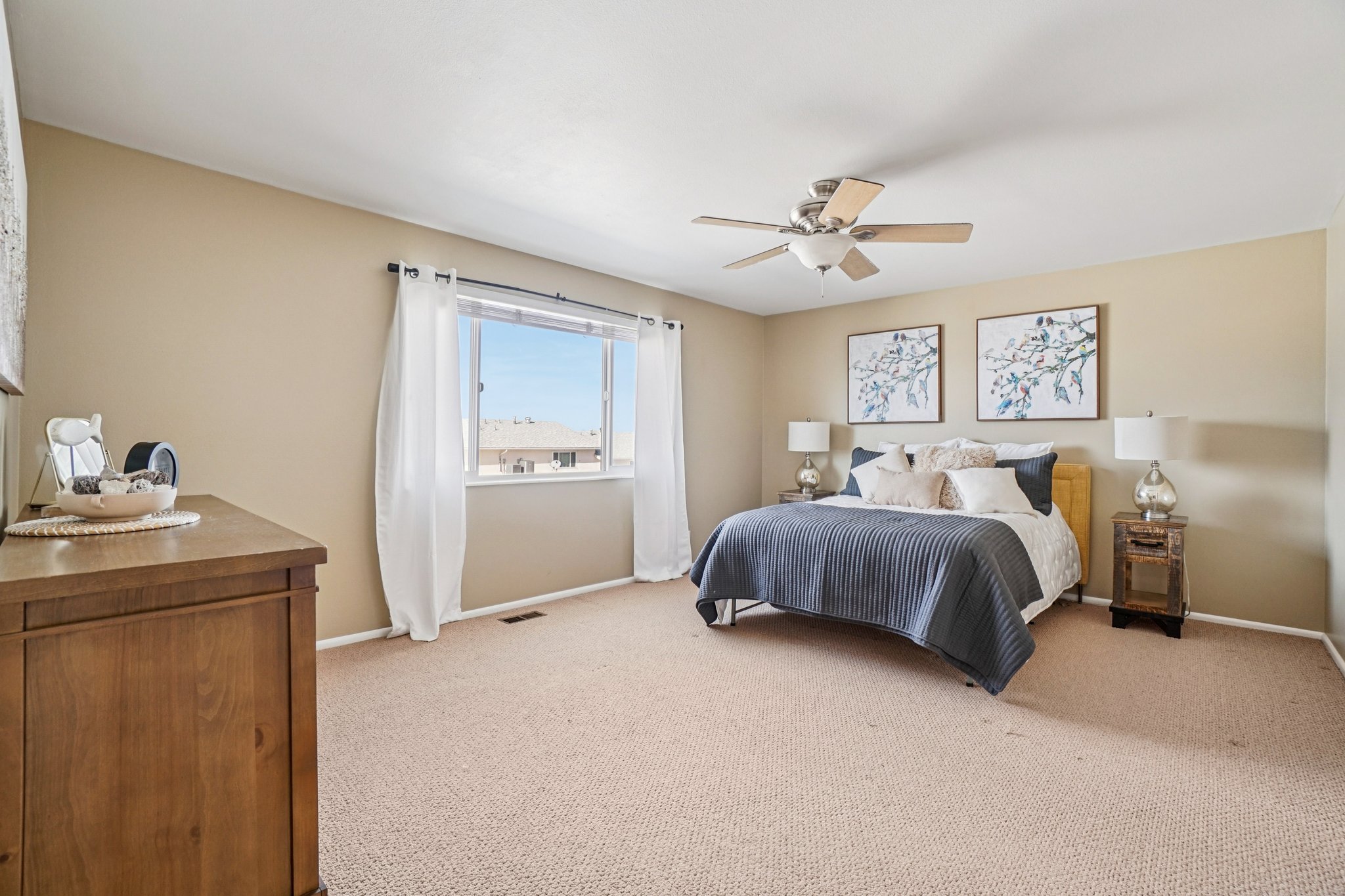 Spacious room featuring neutral wall tones, textured carpet flooring, a ceiling fan with light fixture, and a large window providing natural light